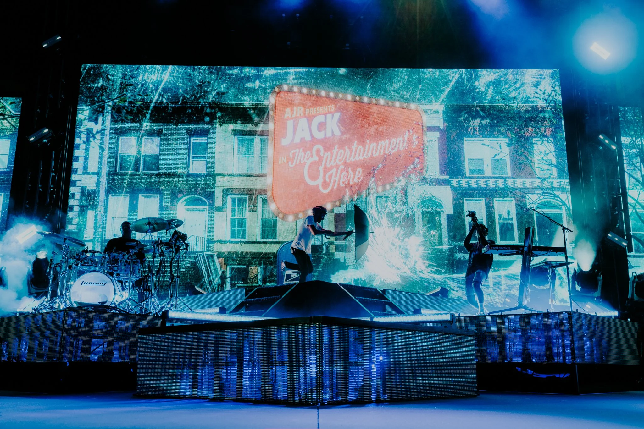 Stage with a large LED screen displaying a movie advertisement for "Jack in the Entertainment Here" and a band performing with instruments and fog effects.