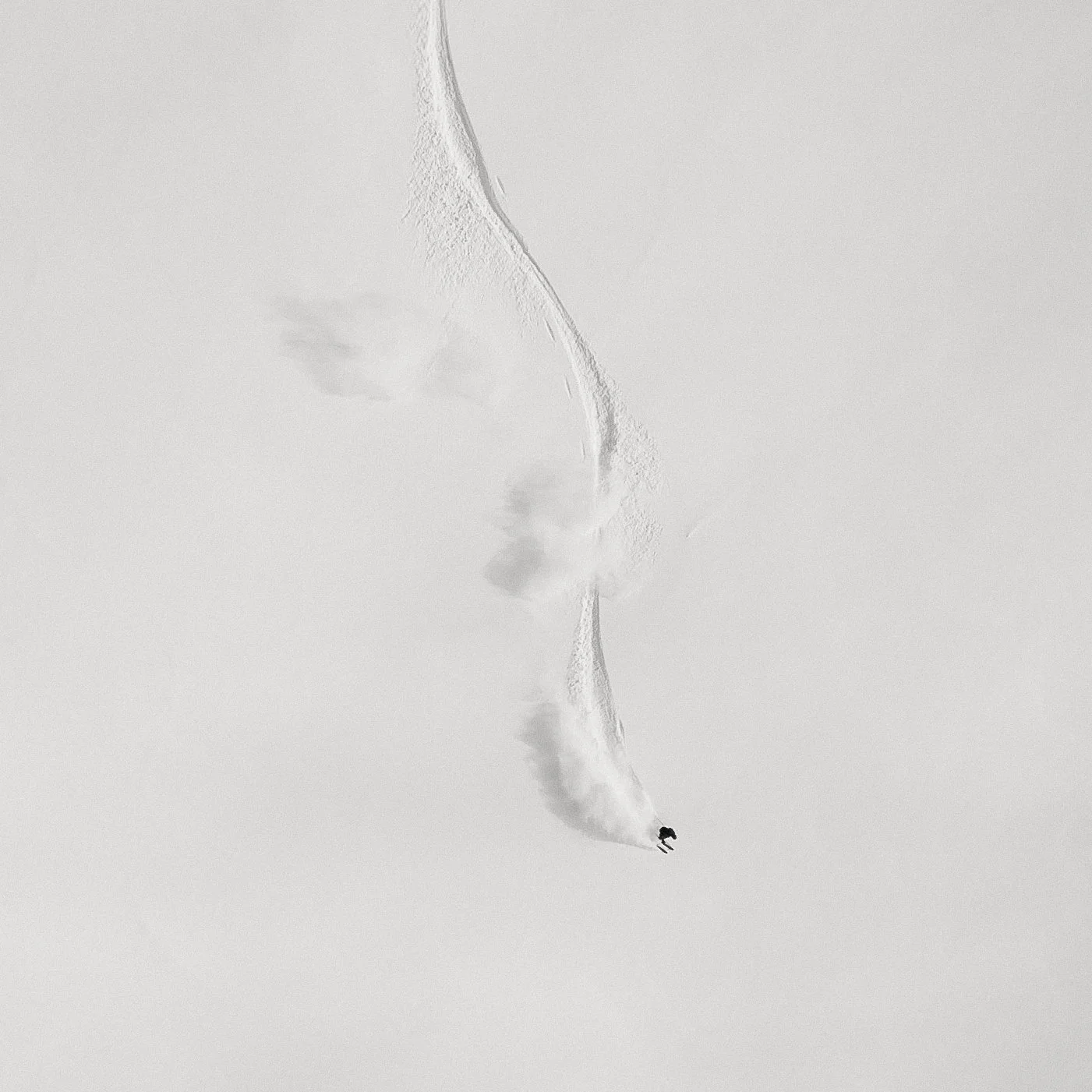 A person snowboarding in a snow-covered landscape, creating a trail of snow behind them.