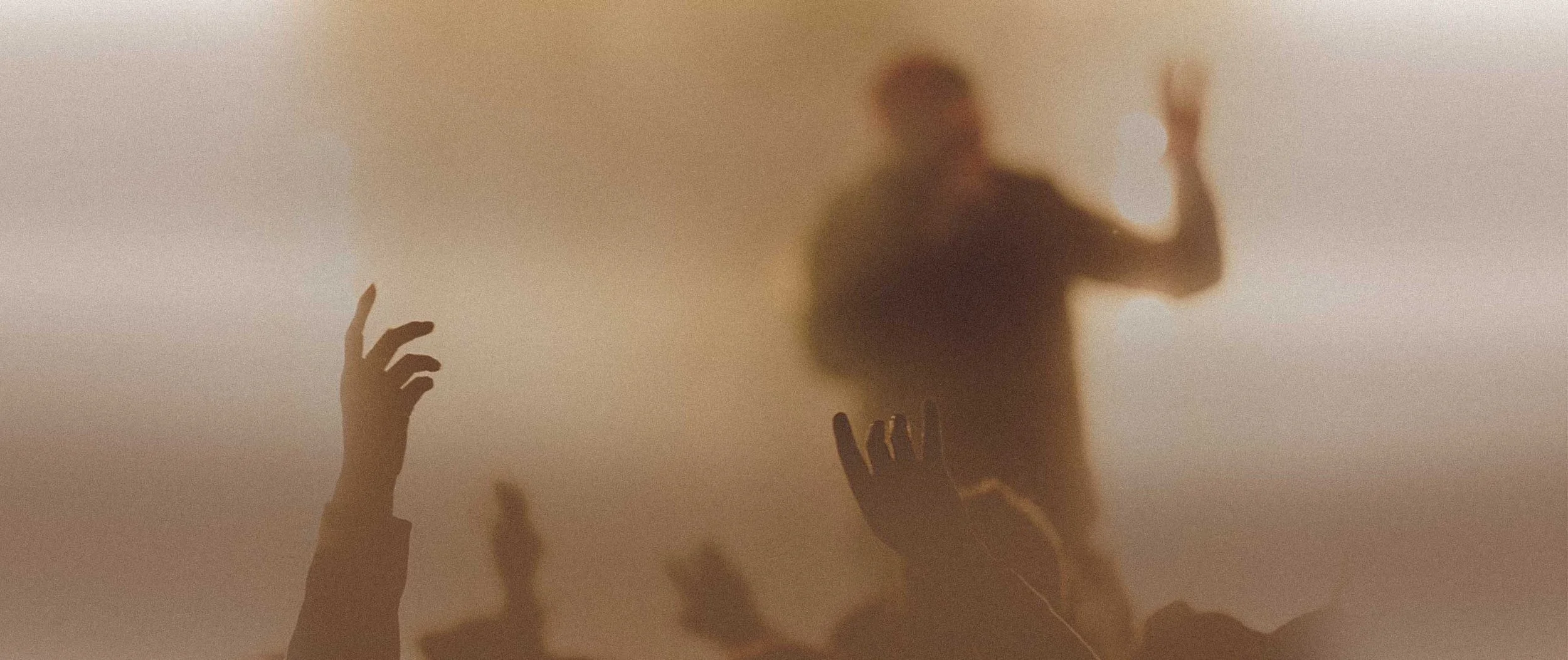 A blurred silhouette of a man with a raised hand is visible through a translucent surface, with hands reaching upward in the foreground.
