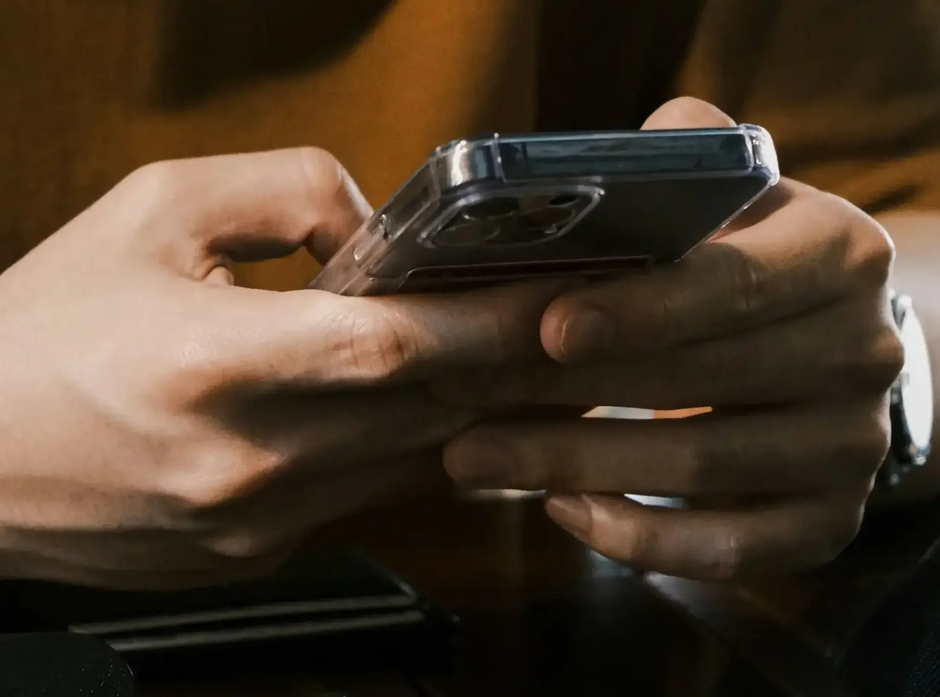 Close-up of a person's hands holding a smartphone, downloading the Door Church App with a background that appears to be a wooden surface or furniture.