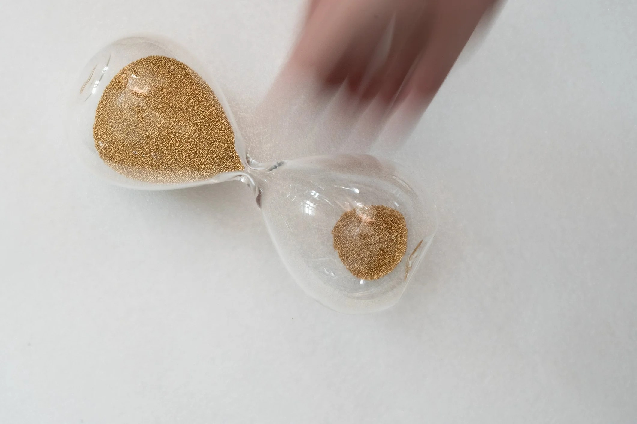 Hourglass on side with blurred hand reaching.