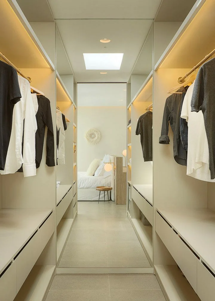 Vestidor con armarios abiertos e iluminación integrada, conectado con el dormitorio.