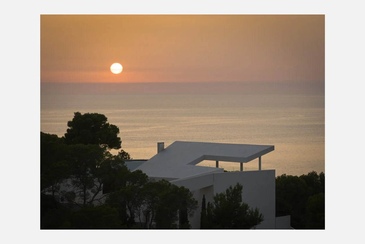 Vista de la cubierta de la villa entre pinos con el sol sobre el mar
