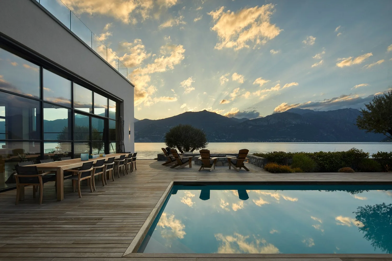 Terraza junto al lago al atardecer, con comedor exterior y nubes reflejadas en la piscina.