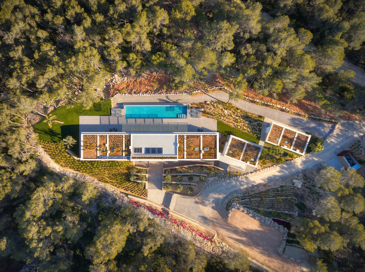 Vista aérea cenital de la villa, sus cubiertas y piscina entre los árboles.