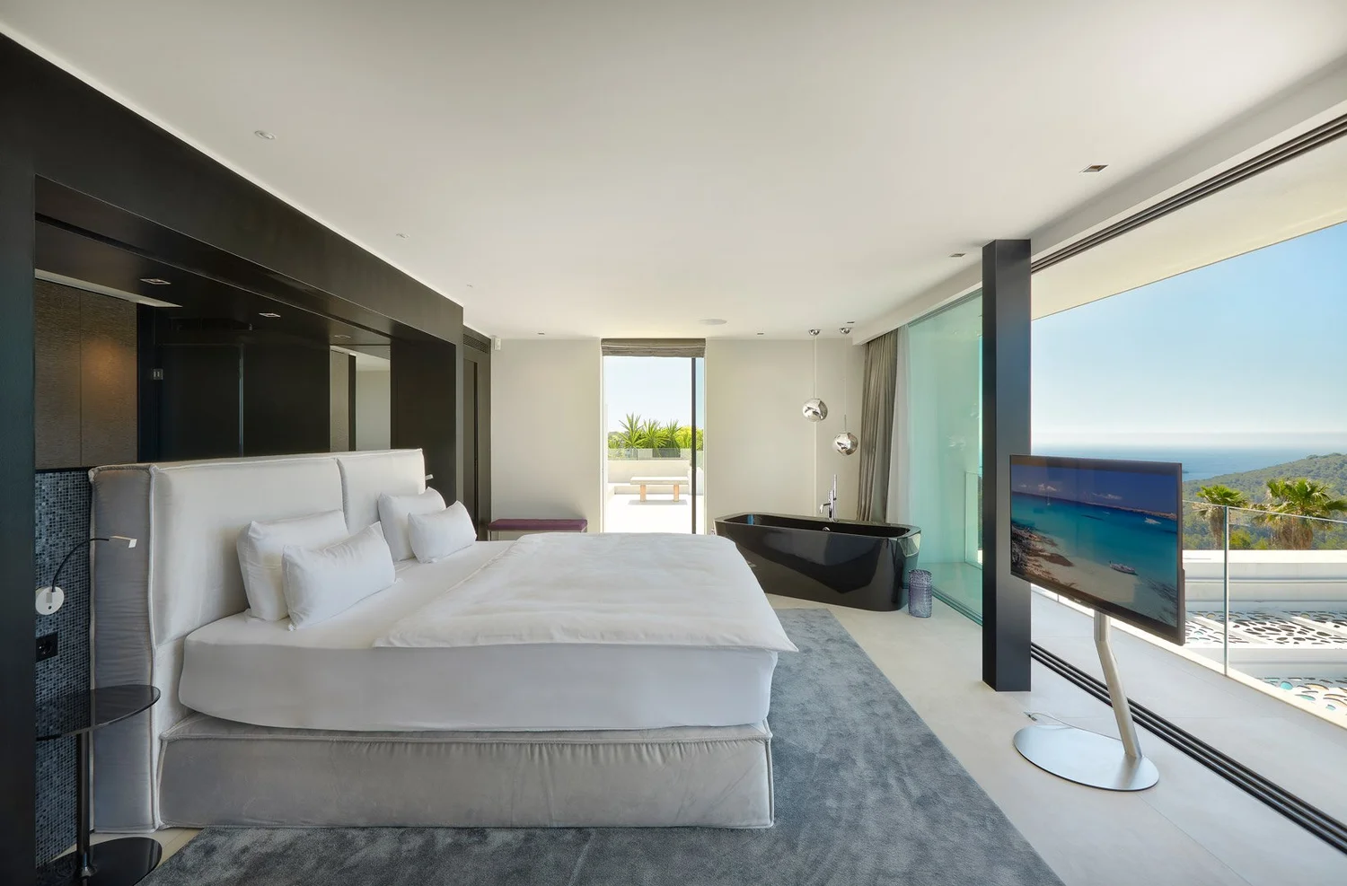 Dormitorio con panelado oscuro, bañera exenta y ventanal hacia el mar.