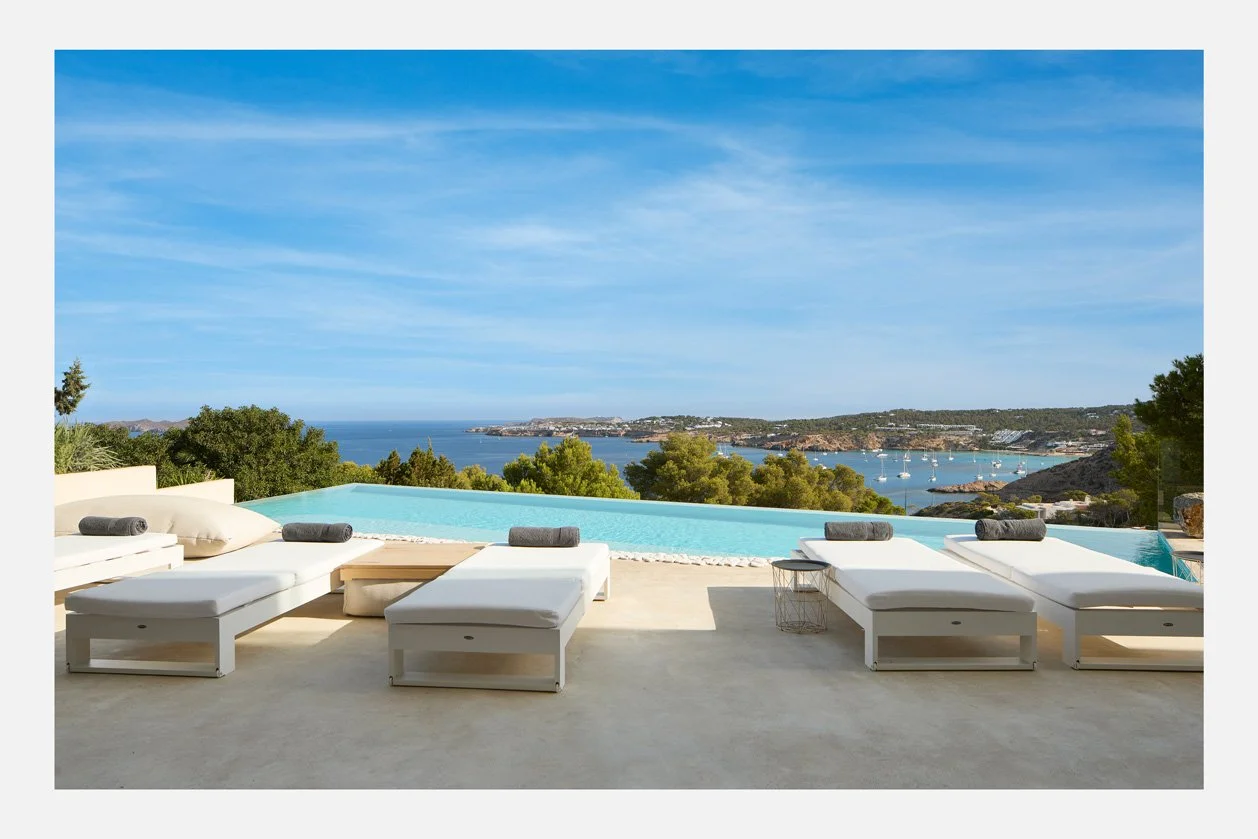 Tumbonas blancas junto a la piscina con vistas a la costa de Ibiza