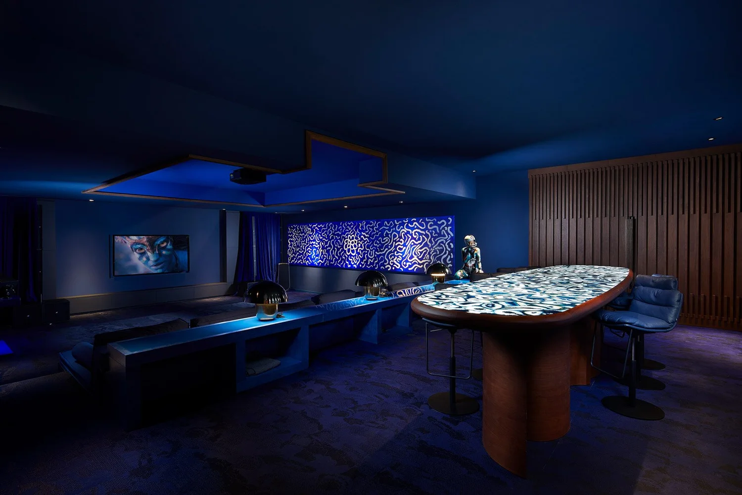 Sala de ocio con barra, taburetes y paneles decorativos bajo iluminación azul.