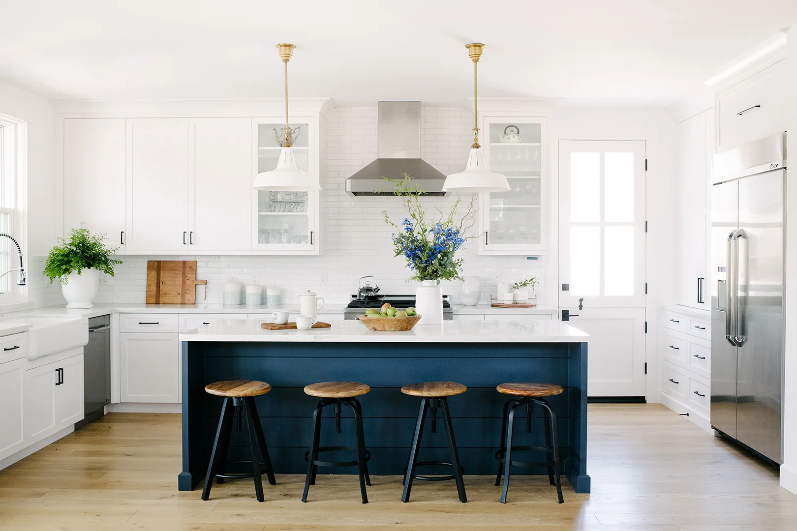 Island pendants by Visual Comfort . Kitchen sink and faucet by Kohler . Drawer pulls by Emtek . Wooden bowl by Kate Lester Home.