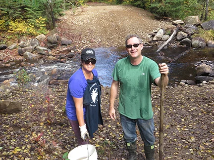 Jen Ashby & Chris Daniels planting shrubs at 10 Mile Creek showing stabilized creek banks as seen in the background with stream flow visible.