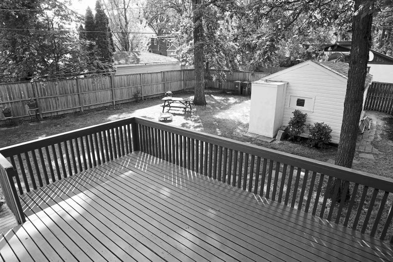 A two-tiered deck overlooks the large yard that is shaded by mature trees.