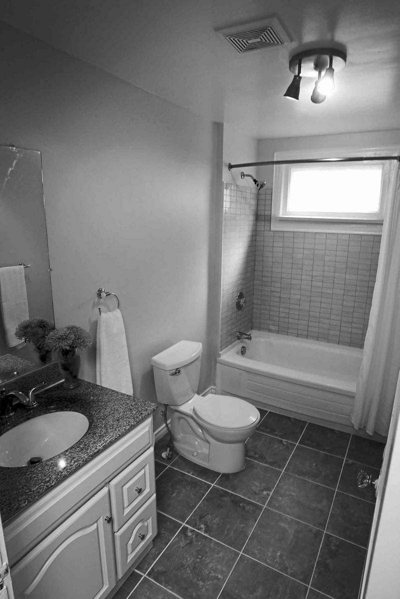 The master bathroom has been updated with grey tile flooring, white vanity and a tub with grey tile surround.