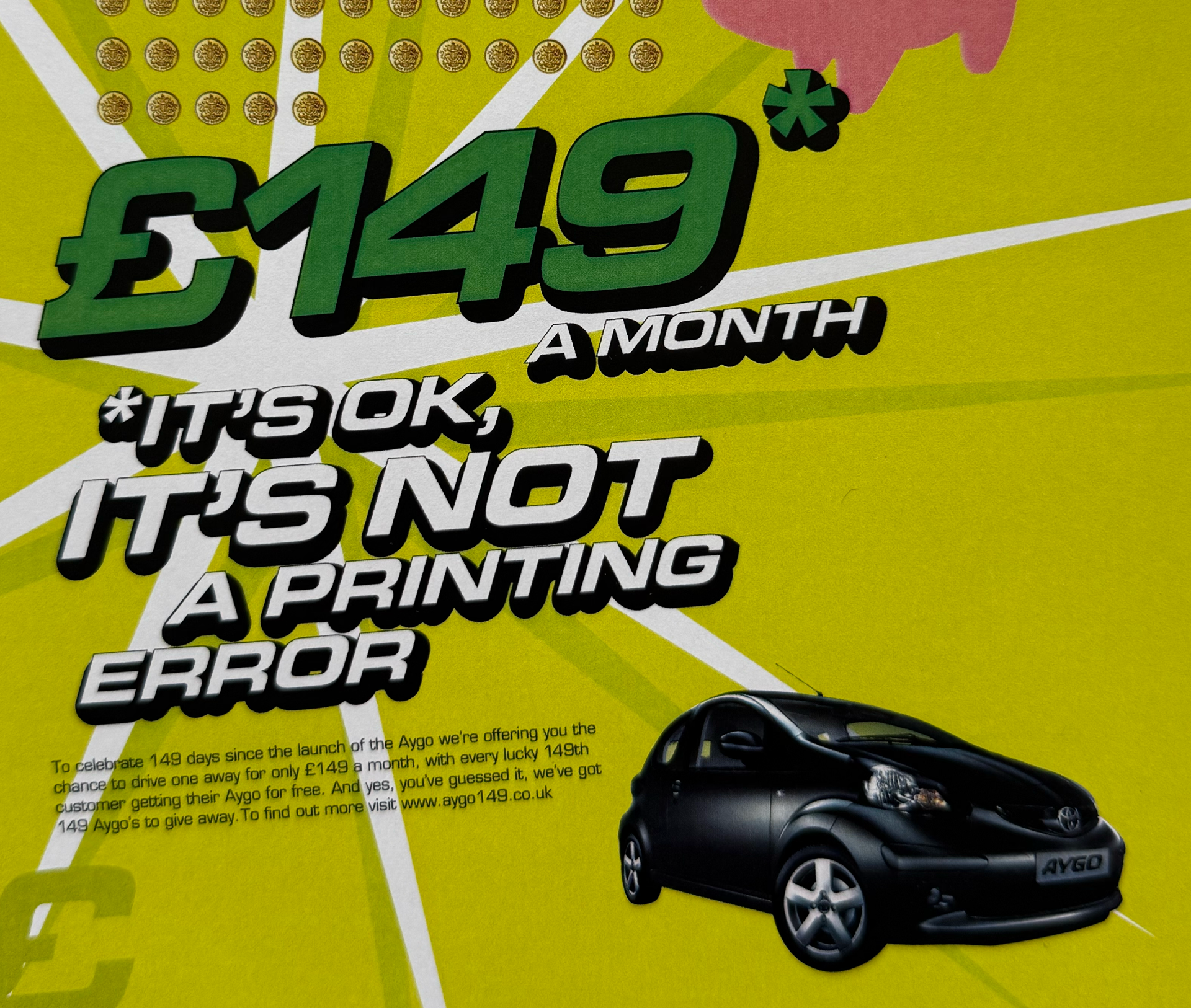 Bright yellow promotional flyer with text in large green and black font announcing a monthly prize of £149, and an image of a black car. The flyer includes smaller text detailing the promotion. Aygo advertising. CHI & Partners.
