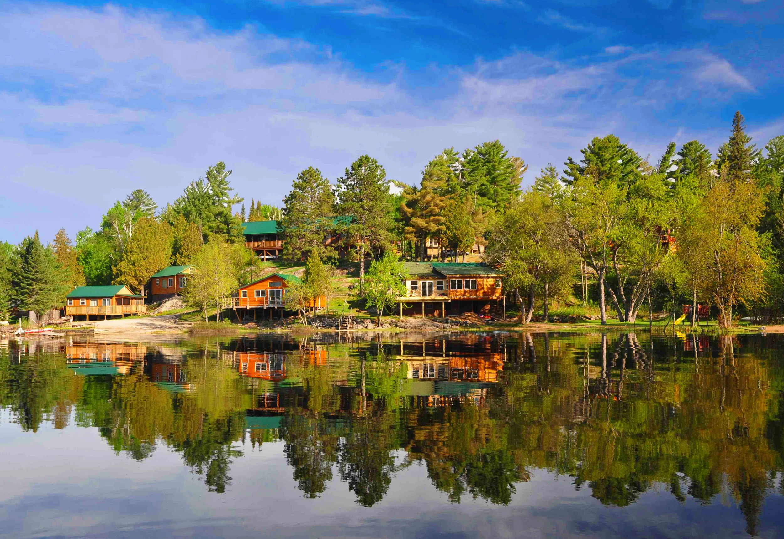 The cabins of Retreats on White Iron Lake reflected in the calm lake among the pines
