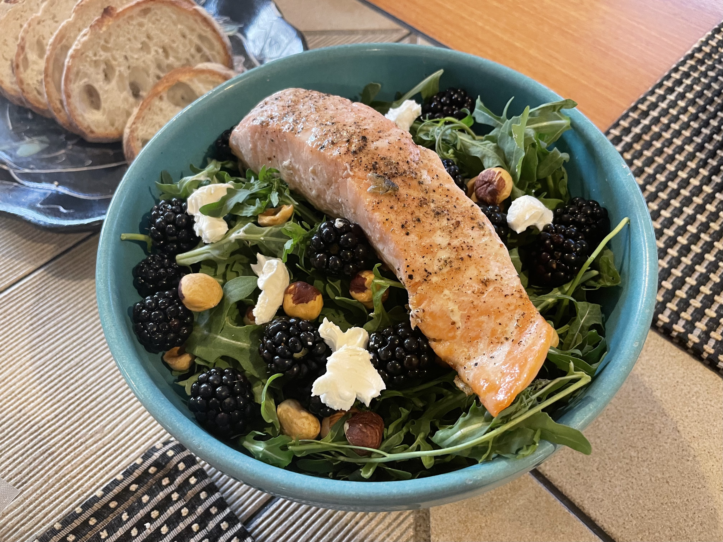 Seattle salad with pan-seared salmon, blackberries, hazelnuts and goat cheese in a ceramic bowl