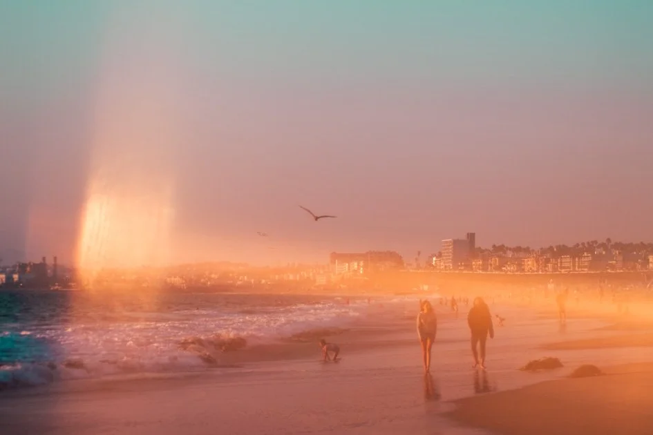 People walking along the beach in warm afternoon light with prism-created reflections and color streaks.