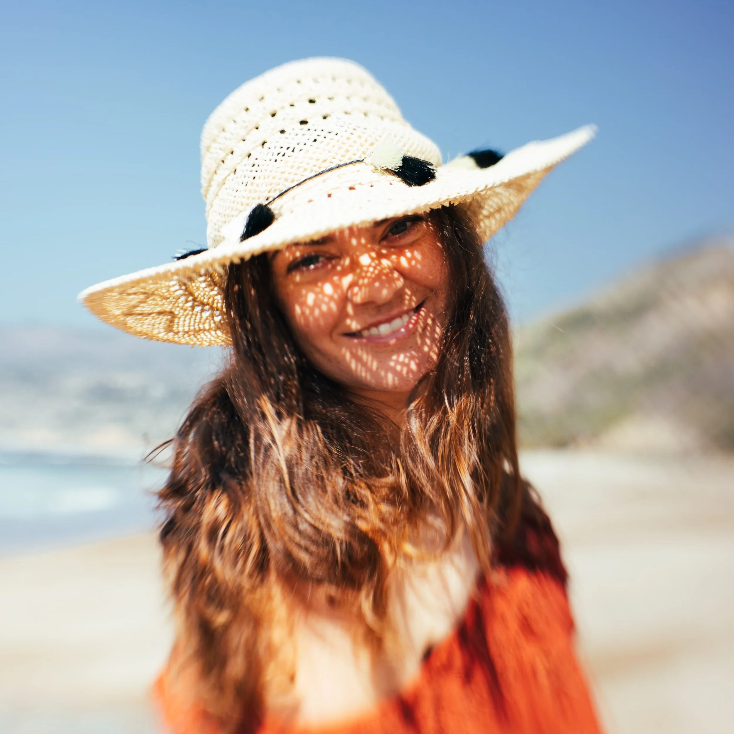 Woman on a beach wearing a straw hat, smiling.