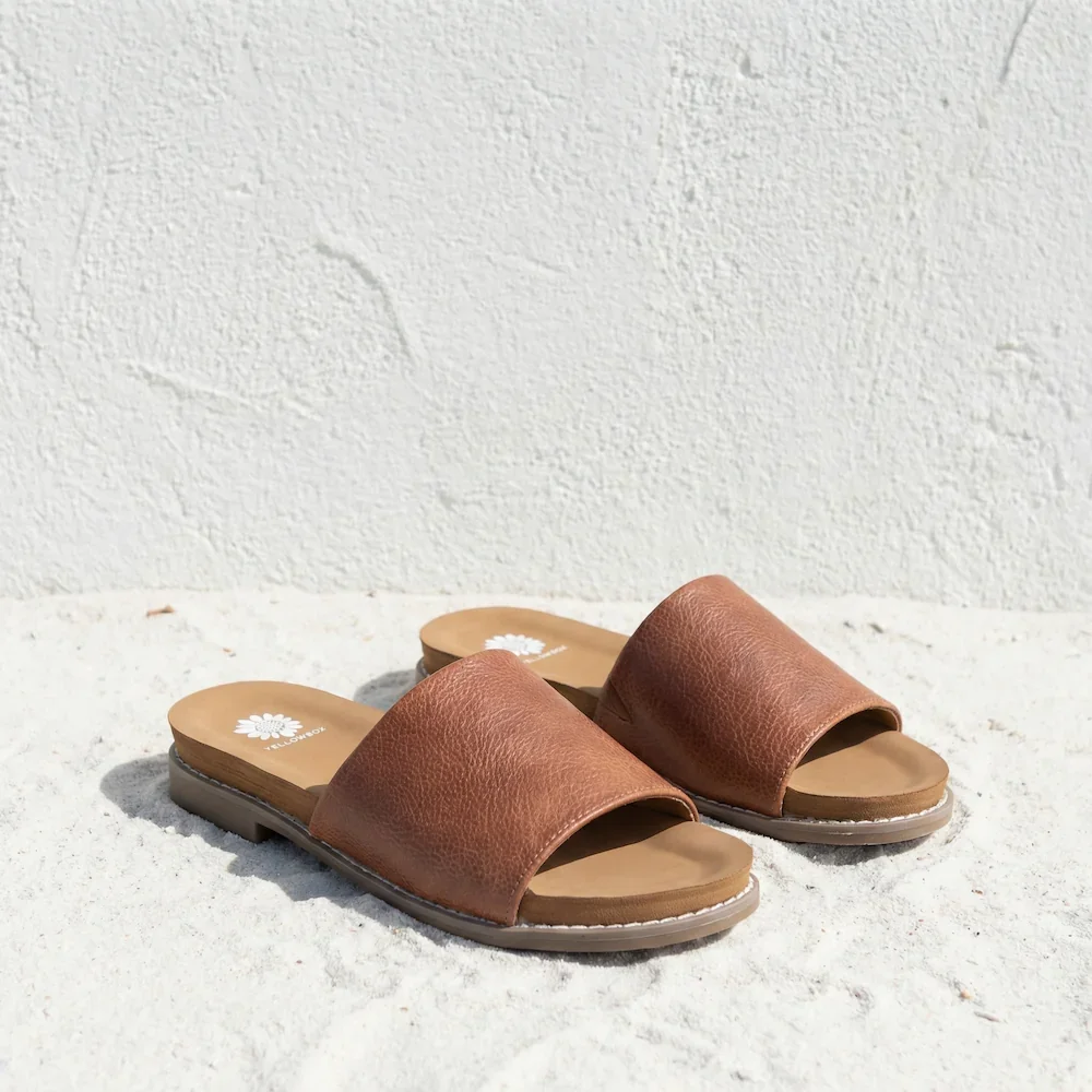 Pair of brown leather slide sandals on a white textured surface.