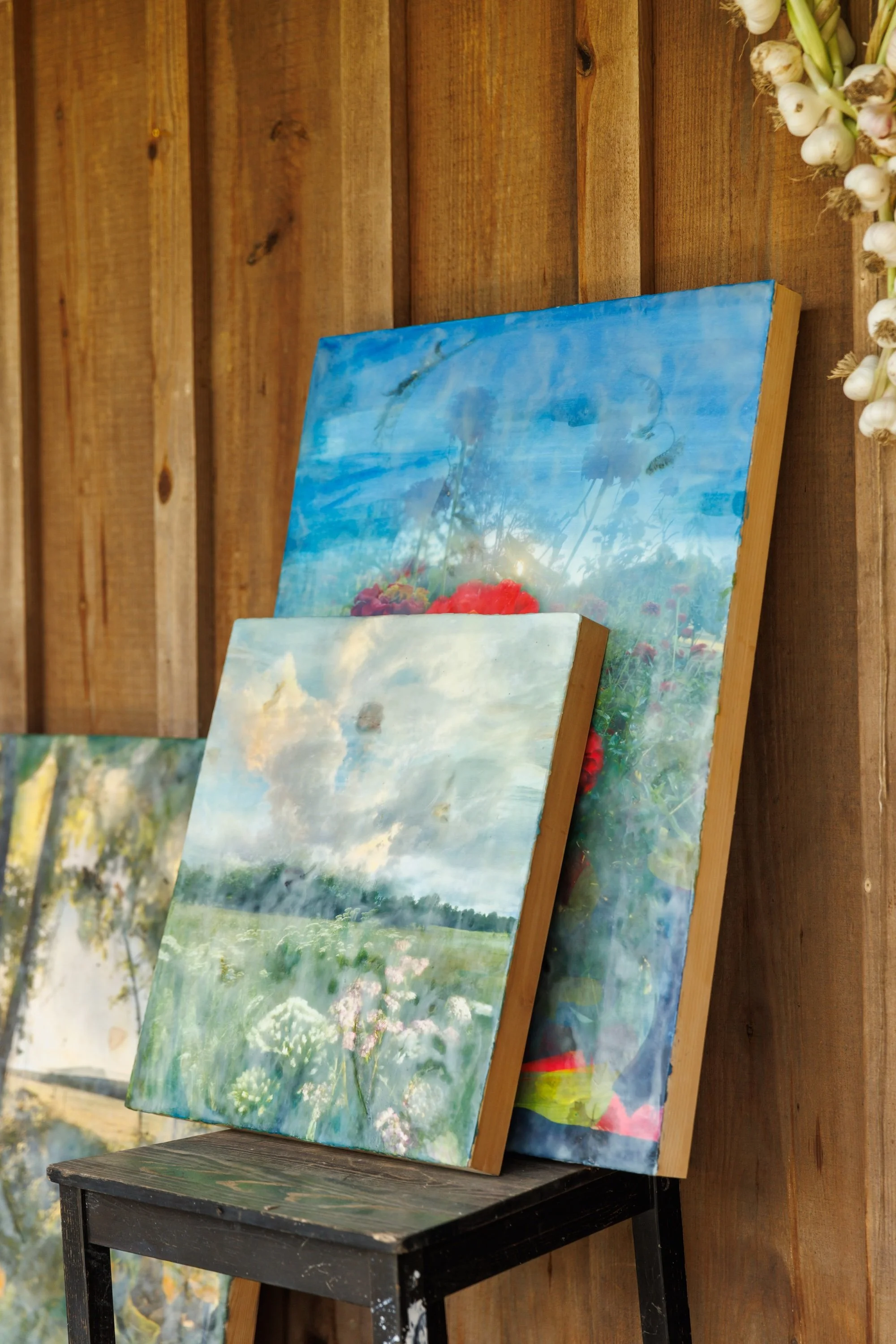 Melissa's landscape paintings leaning on a wooden stool against a barn wall