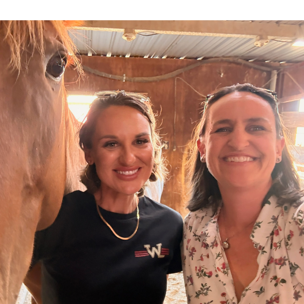 Lily smiling in the barn beside a horse, with the author
