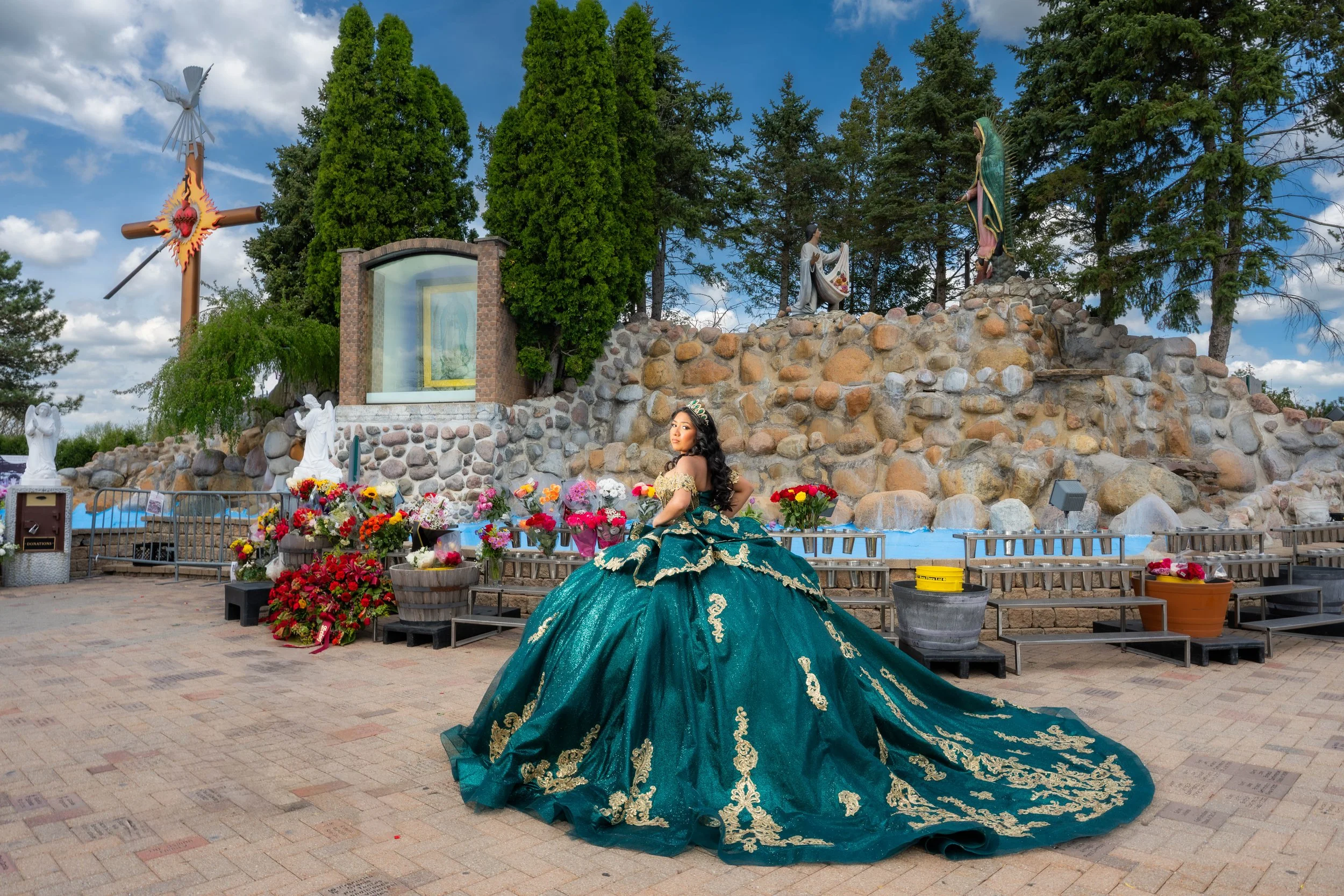 Quinceañera in emerald green and gold quinceañera dress posing at Our Lady of Guadalupe shrine with flowers and religious statues in Chicago