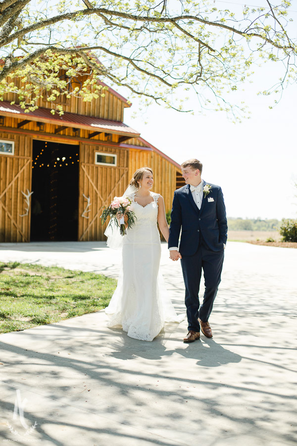 Bride and Groom taking a stroll in front of a rustic barn at the Venue at Waddell Place