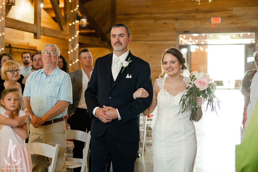 Bride walking down the isle with her father in a rustic barn wedding