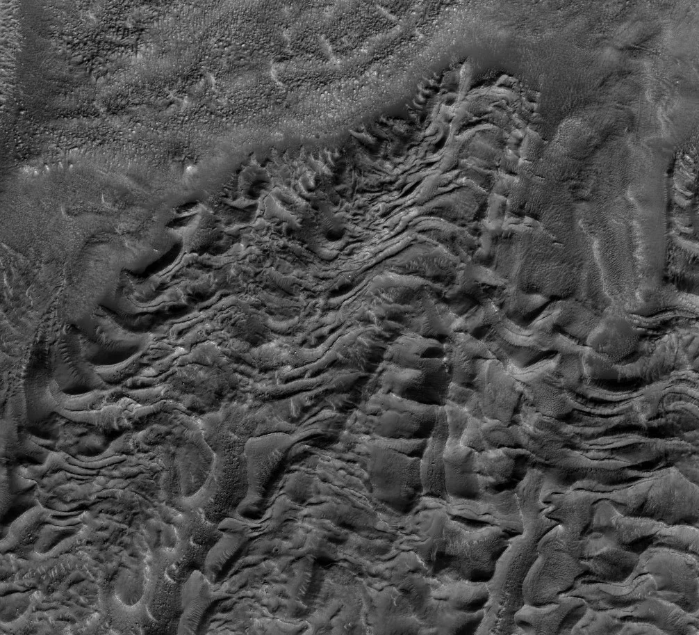 HiRISE image of wavy terrain disrupted by a past moving glacier. 