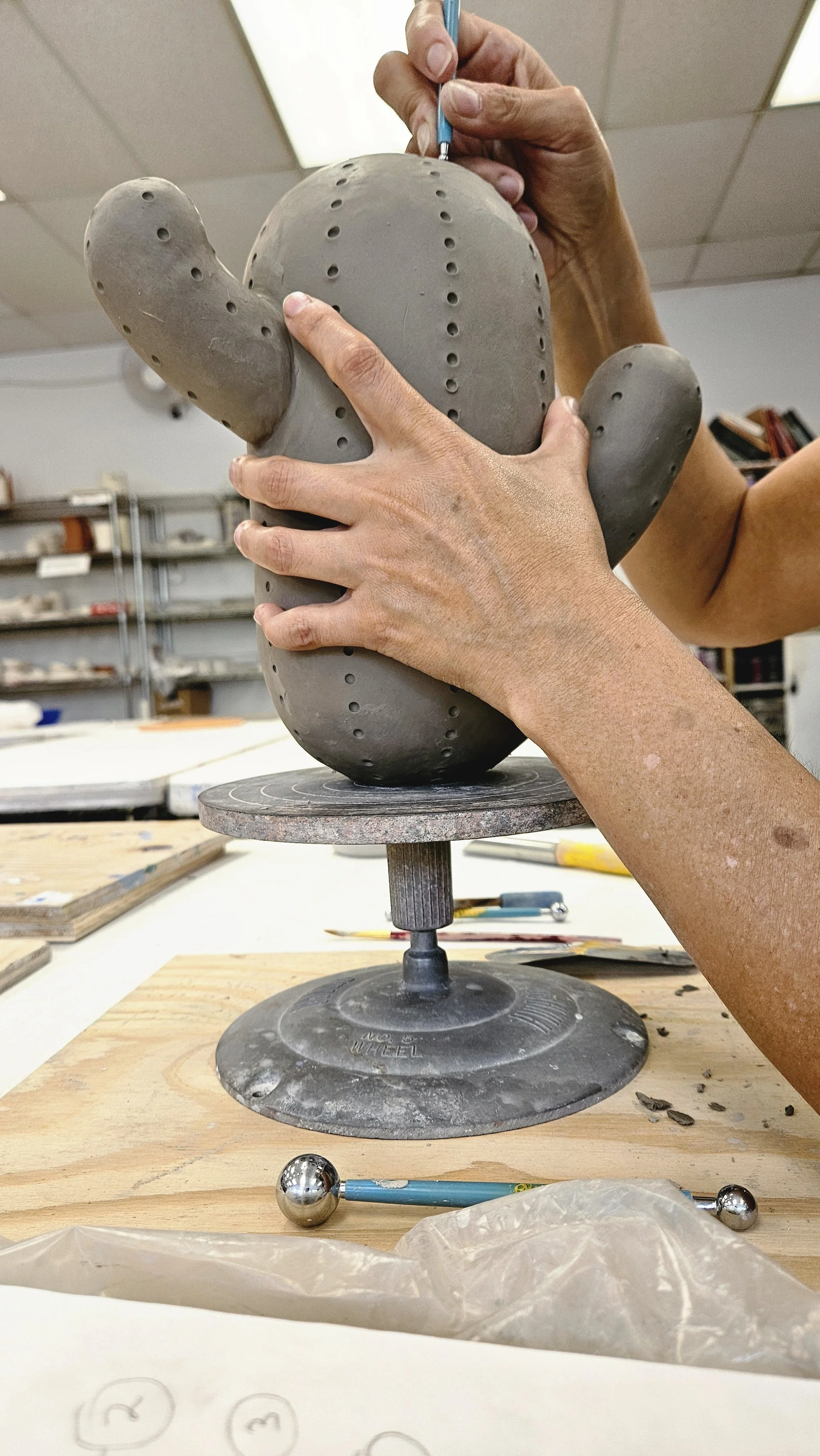 Person shaping a ceramic cactus sculpture in a studio workshop.