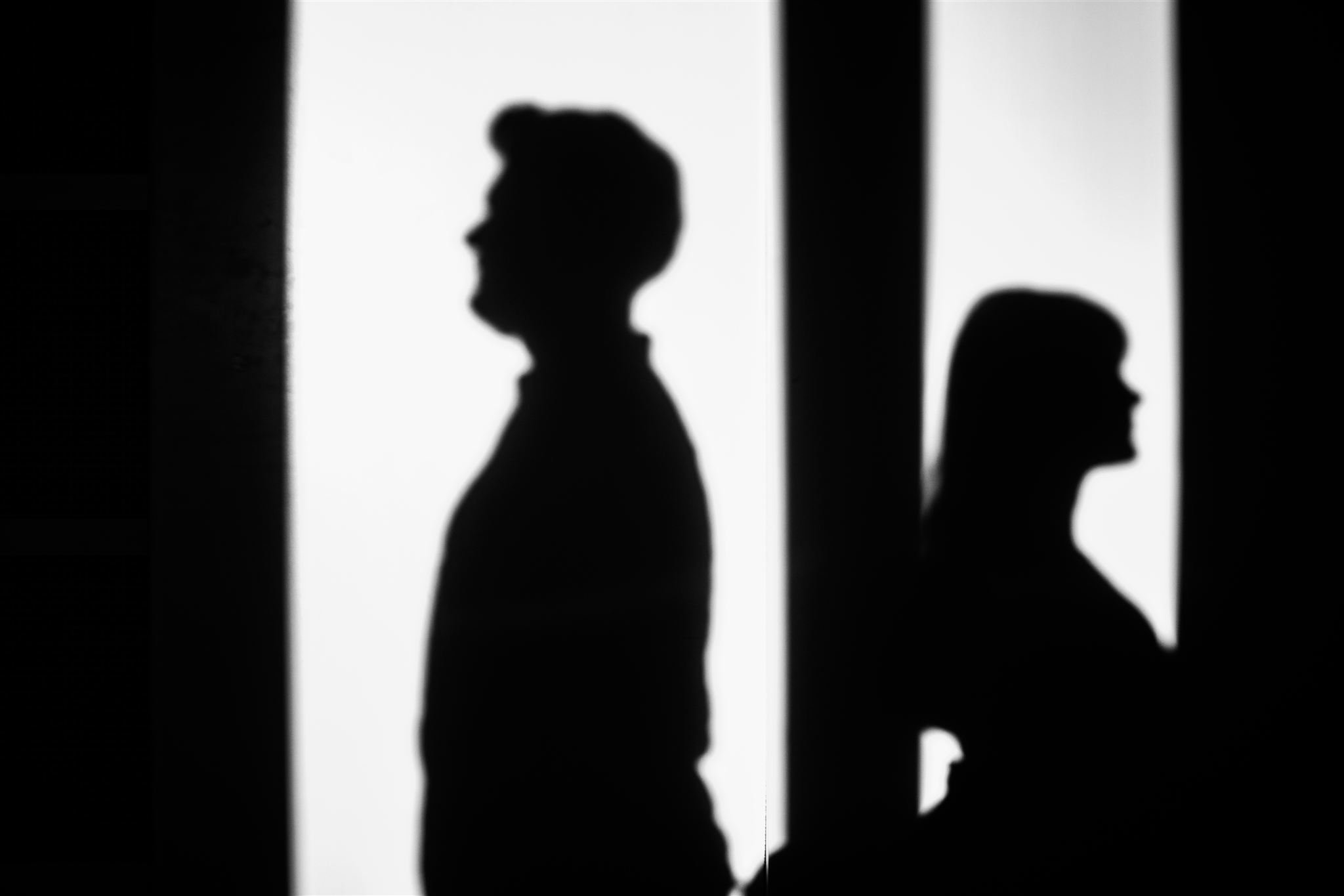 Silhouettes of a man and a woman standing in front of lighted panels, facing opposite directions.
