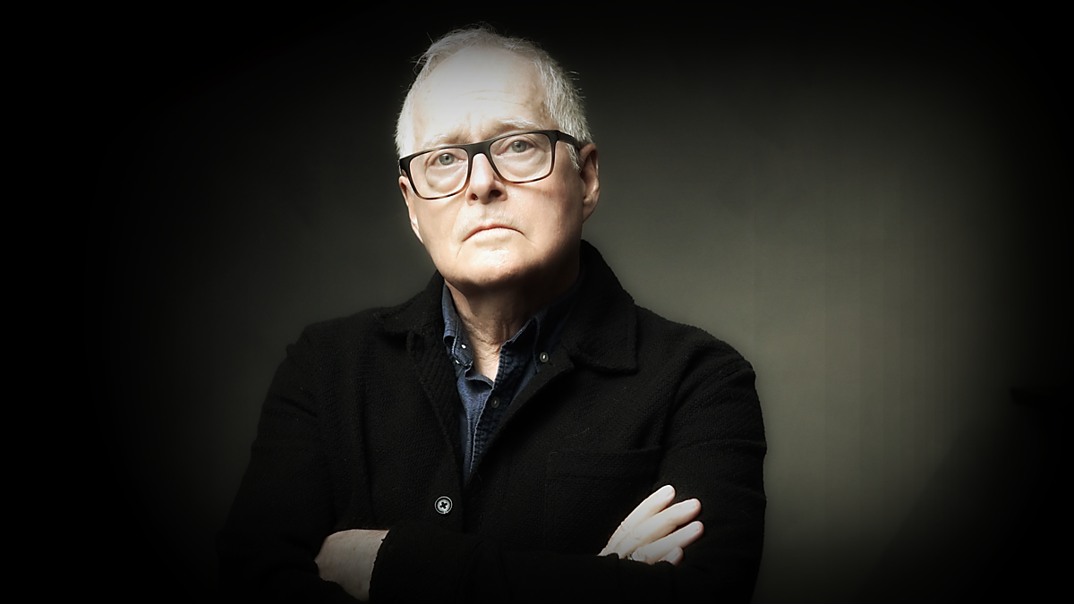 Geoff Edwards looks to camera with his arms folded. He's in a studio with traditional Rembrandt lighting.