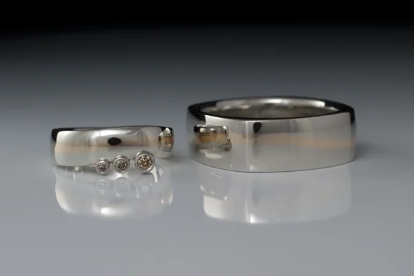 Matching white gold bands with meandering yellow gold stripe inlay with a high polish.  Her band has three bezel set chocolate diamonds. 