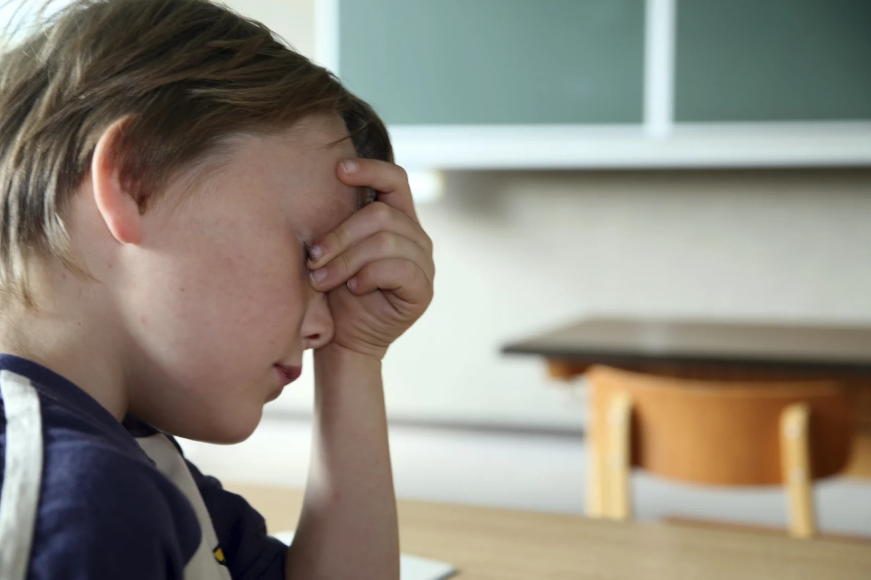 A young child sits in a classroom with his head in his hands