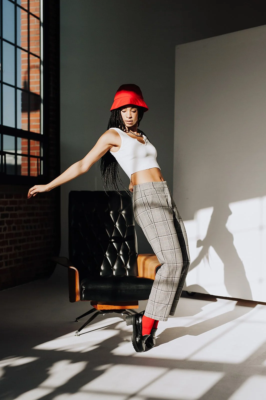 Person in red hat and white top posing by a chair with sunlight casting shadows