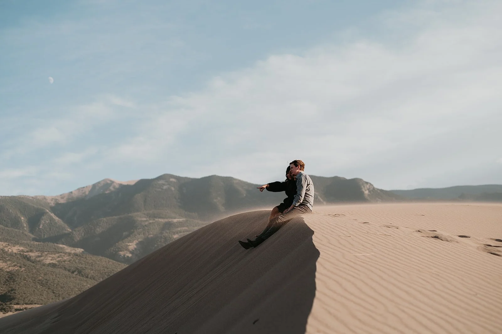 Couple sitting on a sand dune with mountain views
