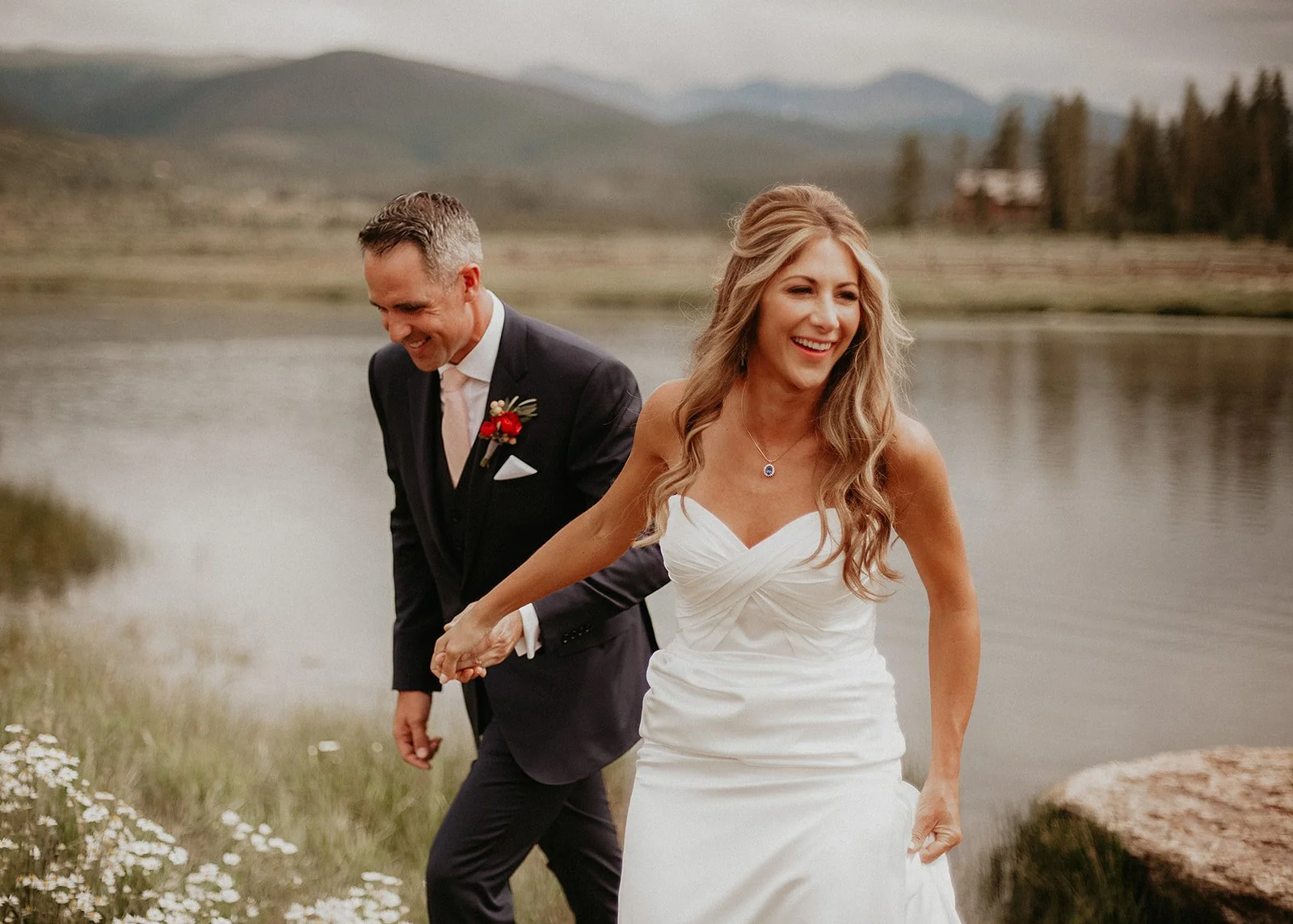 Bride and groom hold hands by the lake