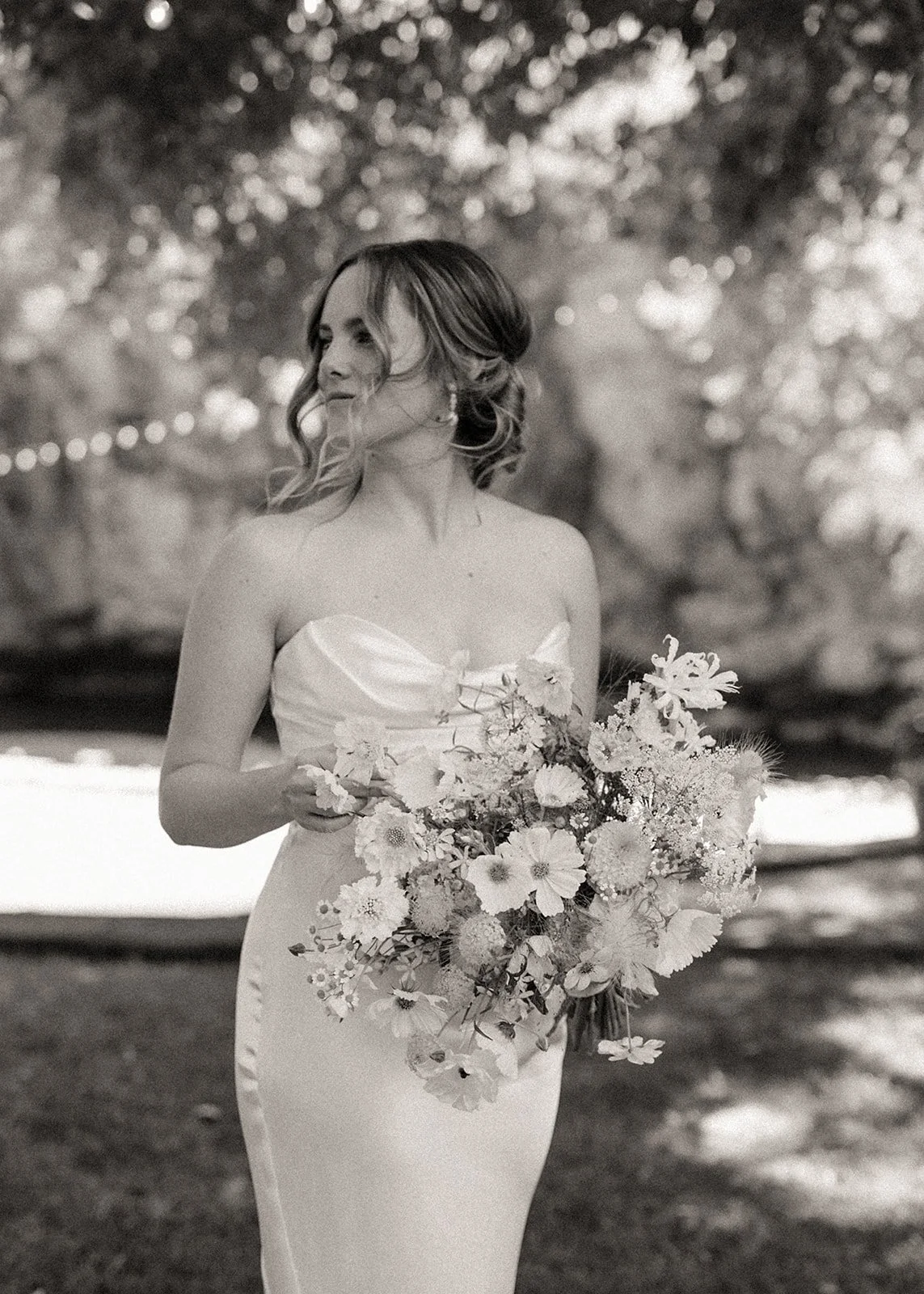 Black and white photo of a bride holding a bouquet of flowers outdoors.