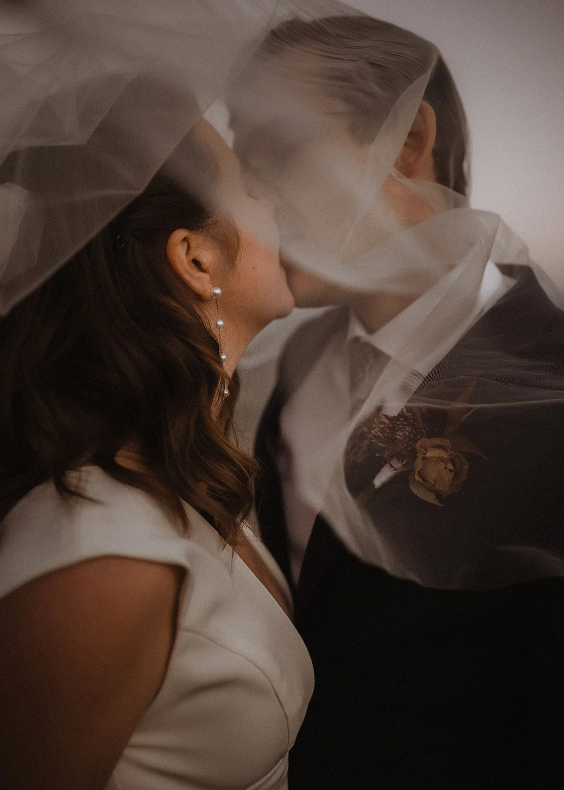 Close-up of a bride and groom kissing under a veil.