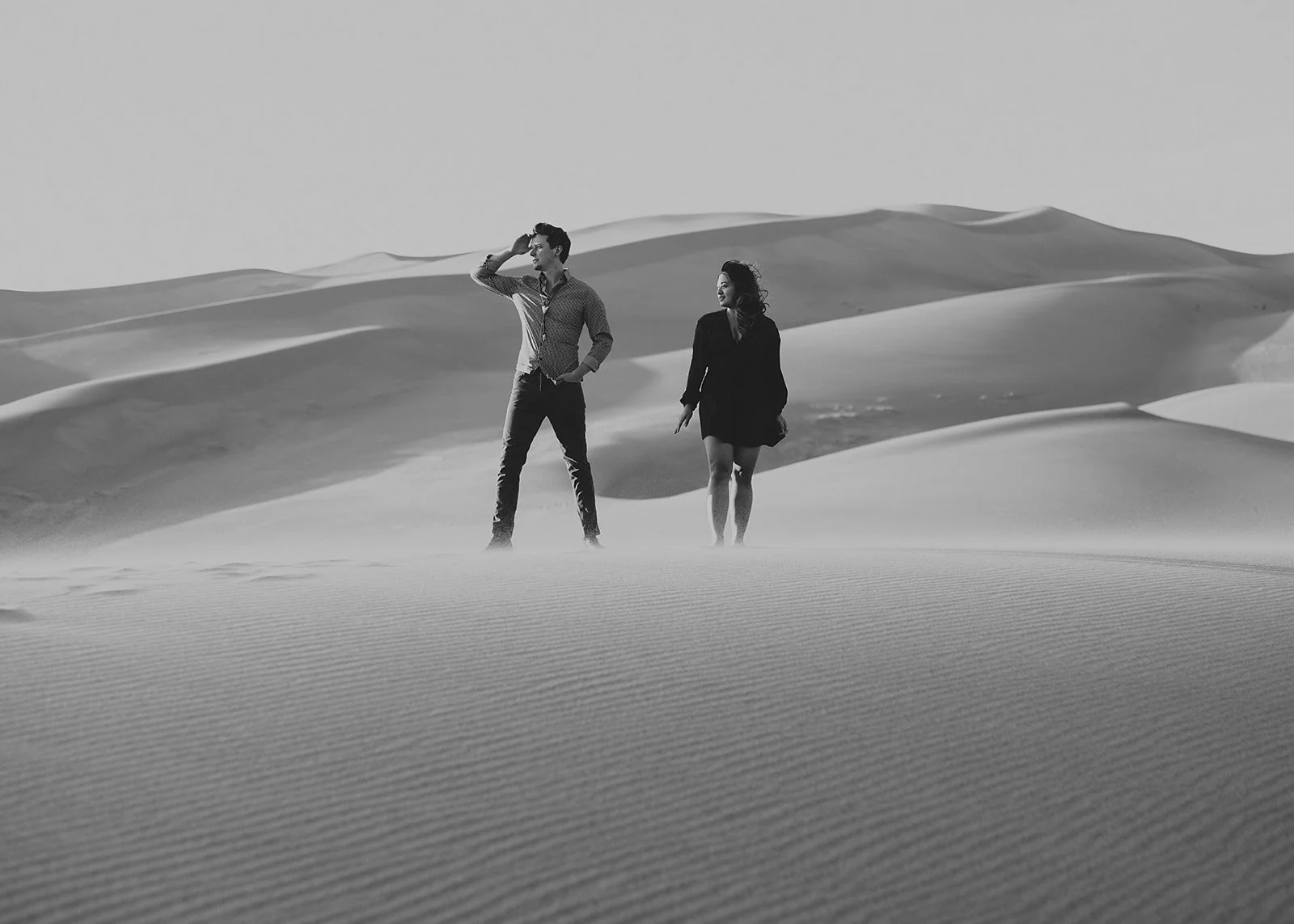 Two people walking in a desert with sand dunes, black and white photo.
