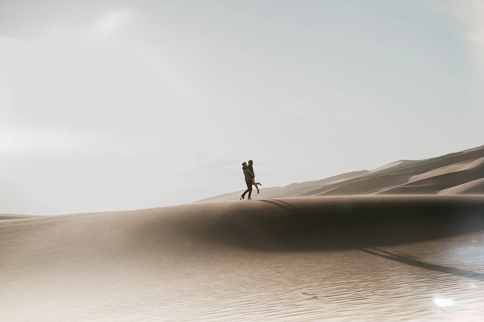 Couple embracing on sand dunes under a clear sky.