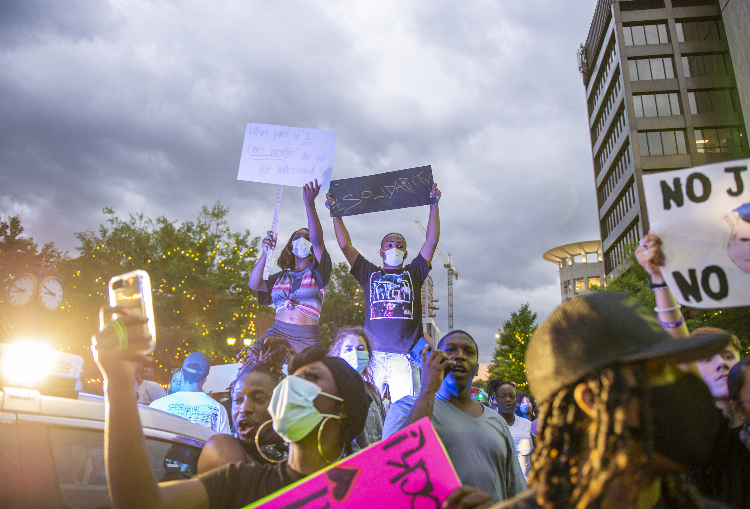 Two protesters stand on top of a police vehicle as officers surround the crowd to create a barricade.