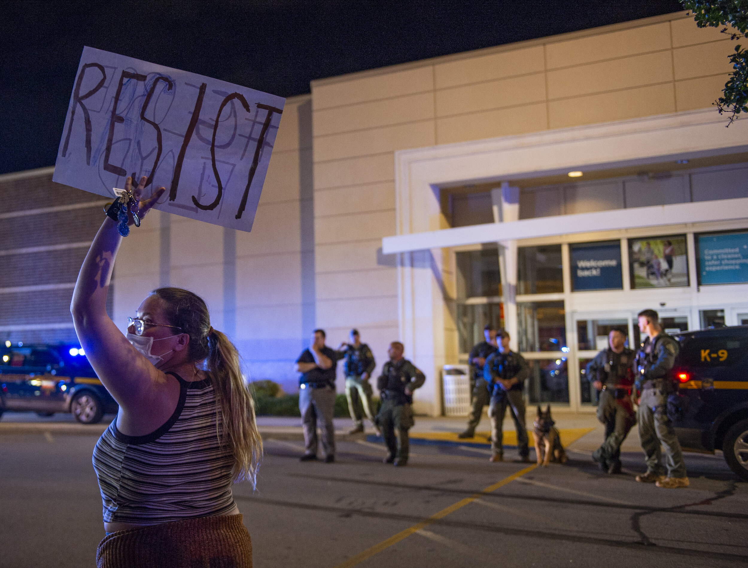 As protesters disperse a woman stands in front of police officers and holds up a sign refusing to leave.