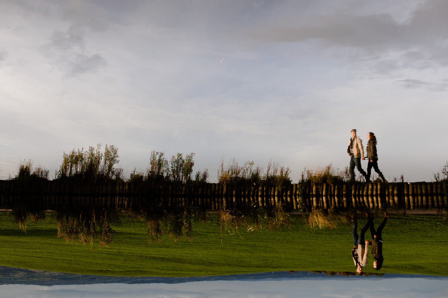 Flipped reflection of a couple walking alongside a lake - Merseyside wedding photography