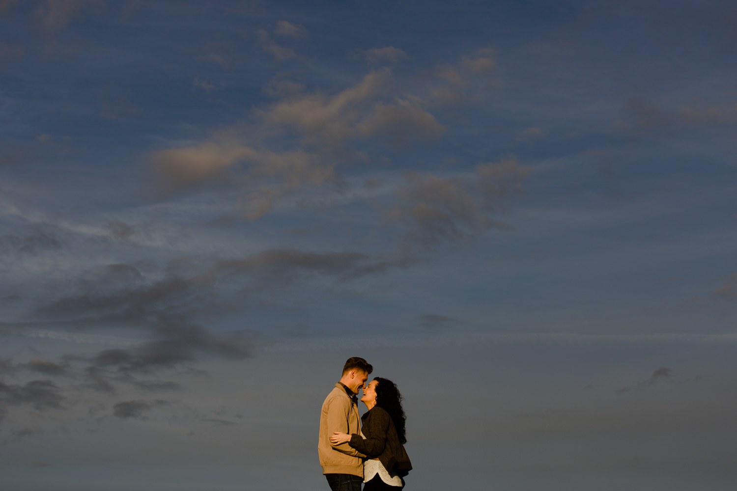 A couple laugh together against the golden hour sky