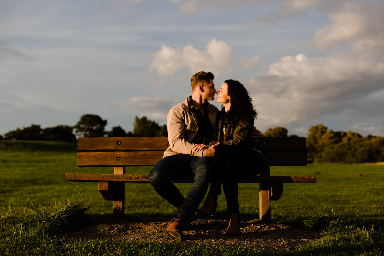 A couple close together on a bench at sunset