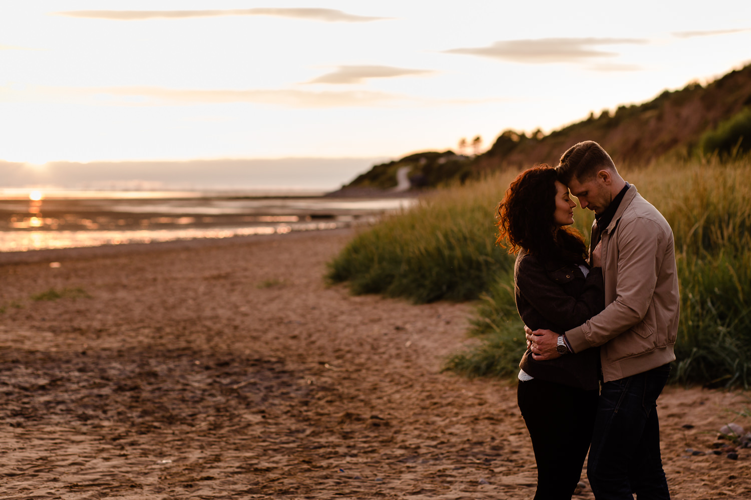 A couple with their heads leaning on each other at sunset on a beach in Wirral