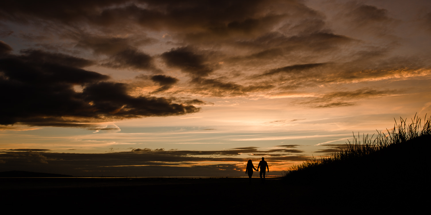 Couple walking towards the sunset, silhouetted against the sky - Merseyside