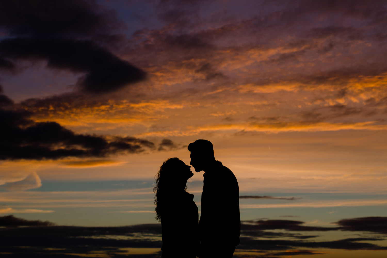 Colourful sunset sky with a silhouette of a couple on their pre wedding shoot - Merseyside Wedding Photographers