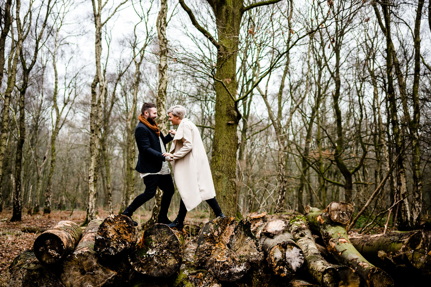 Couple climb on a pile of logs on a woodland engagment shoot, Yorkshire wedding photographer