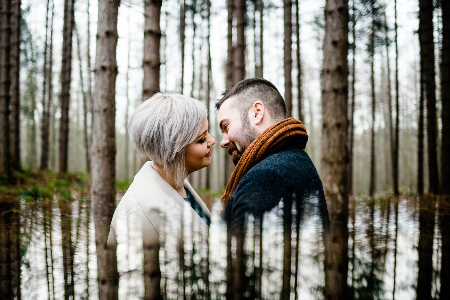 Engaged couple almost kissing surrounded by pine trees with reflection, wedding photographer in Yorkshire